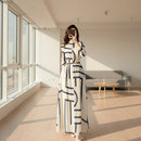 Person wearing a white dress with blue geometric patterns, standing in a room with abstract art on the wall.
