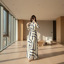Woman taking a mirror selfie wearing a long dress with geometric pattern in a modern room.