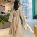 Woman in a beige trench coat walking in a modern cafe.