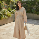 Woman in a beige trench coat holding an umbrella in a modern interior setting