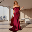Woman in a burgundy evening gown standing against a dark background with a red couch.