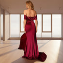 Woman in a burgundy evening gown standing in a dimly lit room with a red couch.