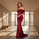 Woman in a burgundy off-shoulder gown standing against a dark background