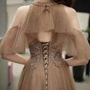 Beige evening gown with intricate detailing and sheer sleeves.