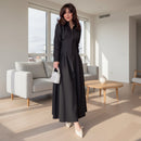 Woman in a black dress standing in a room with wooden flooring and a glass table.