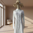 Mannequin wearing a white dress with a straw hat against a tiled wall.