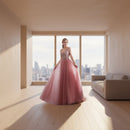 Pink evening gown with beaded top on a model against a white curtain background