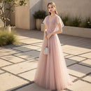 Woman in a pink evening gown standing against a textured gray wall.