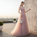 Woman in a pink evening gown standing against a textured gray wall.