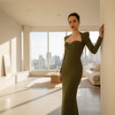 Woman in a green dress posing against a plain wall.